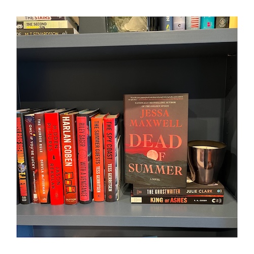 A copy of dead of summer next to other red books and a black candle