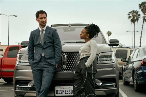 The Lincoln Lawyer on Netflix: Mickey with new character Izzy, played by Jazz Raycole. In the photo, Izzy and Mickey lean on one of Mickey's Lincolns.