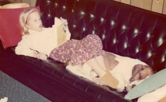 Jen at age ten or eleven reading a Nancy Drew book on a black leather couch with a brown and white hound dog sleeping at her feet.