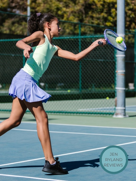 Young girl in a green and blue tennis outfit hitting a ball on a tennis court
