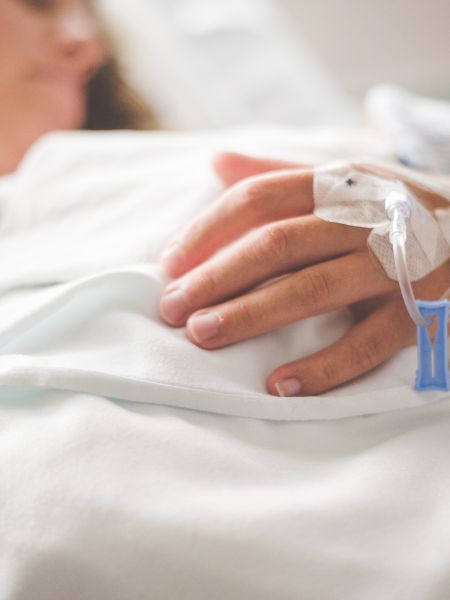 A patient with an IV in their hand lies in a hospital bed.