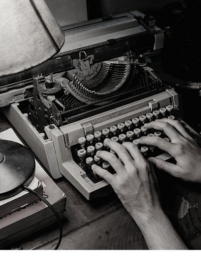 Person typing on a antique typewriter in a black and white photo