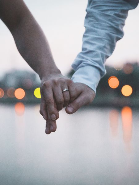 Couple holding hands in front of a body of water, which could be the ocean or a bay.