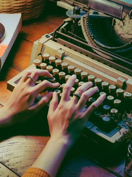 Verity by Colleen Hoover is about a writer. Photo of a woman typing on an old fashioned typewriter