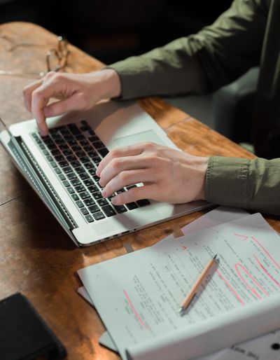 Hands typing on a laptop with a manuscript