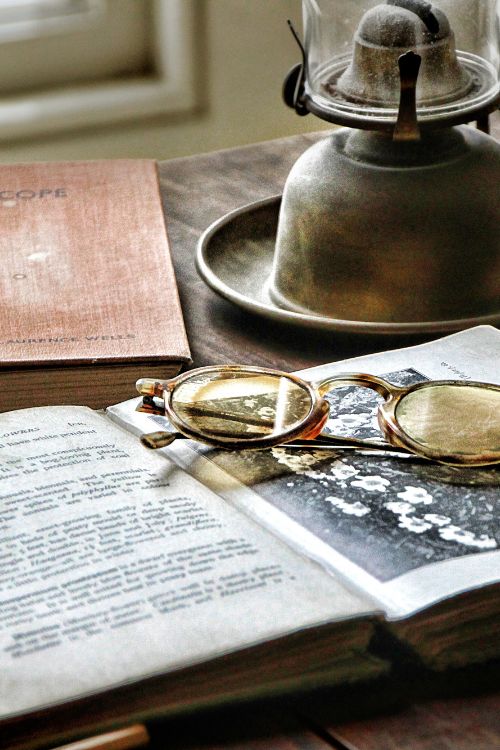 Vintage looking photo of items on a deck: an oil lamp, an old book, and a pair of antique spectacles.