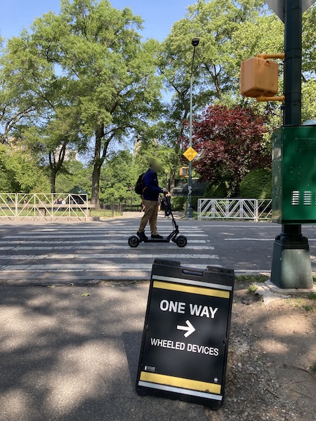 Photo of a person on an electric scooter riding through a crosswalk on the Central Park road. Photo by Jen Ryland LLC.