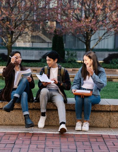 Photo of three students sitting on a stone bench looking at textbooks.