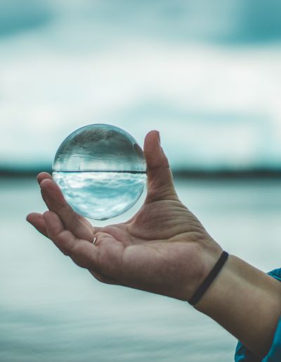 A hand holds a crystal ball. The hand is in front of a blue background of sea and sky.,