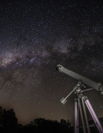 At night, a figure stands beside a telescope set up to look at the stars