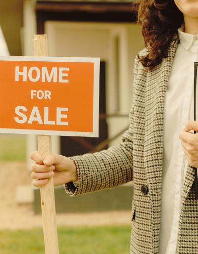 Woman sticking a for sale sign in the lawn of a house