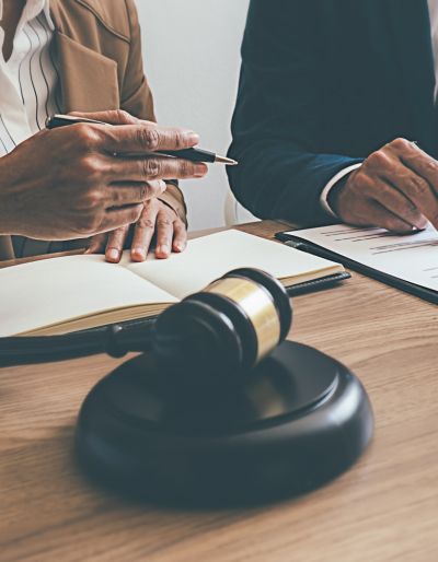 Two people in suits sitting next to each other at a table with a judge's gavel in front of them.