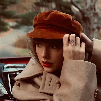 Taylor's Red Album cover feasting her in a camel coat, dark orange newsboy cap, and ornate gold ring. She's wearing red lipstick.