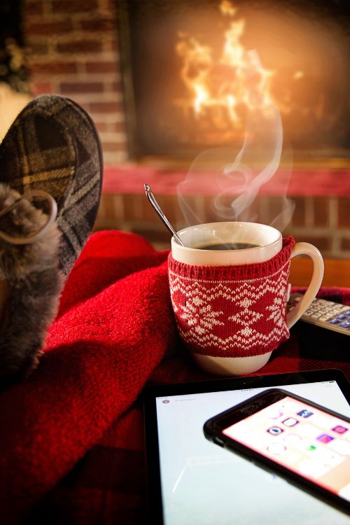 Photo of a person reading by a fire with a steaming mug next to them.