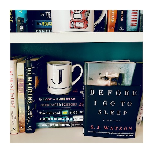 Photo of a hardcover of Before I Go To Sleep on a bookcase with other psychological suspense books and a J mug