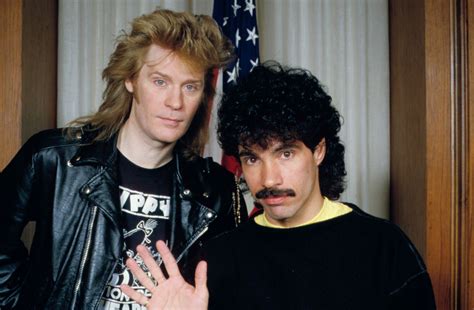 A photo of Daryl Hall and John Oates in front of an American flag on a stand