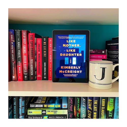Original photo of Like Mother Like Daughter. The book's cover features a house at night with one window illuminated and is on a bookcase with red books and a J mug