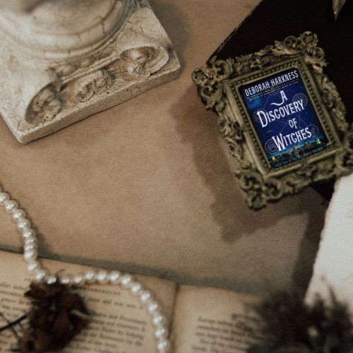The cover of A Discovery of Witches in an antique picture frame next to a sculpture, a string of pearls and an old book