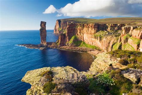 Photo of Orkney, UK. A rugged coastline with steep cliffs against a blue ocean