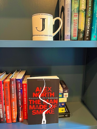 A Man Made of Smoke by Alex North on a blue bookcase with other books and a J mug