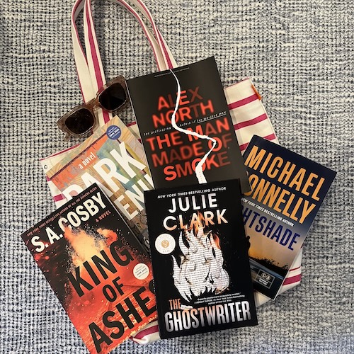 Five hot books of Summer 2025 on a striped tote with a pair of sunglasses