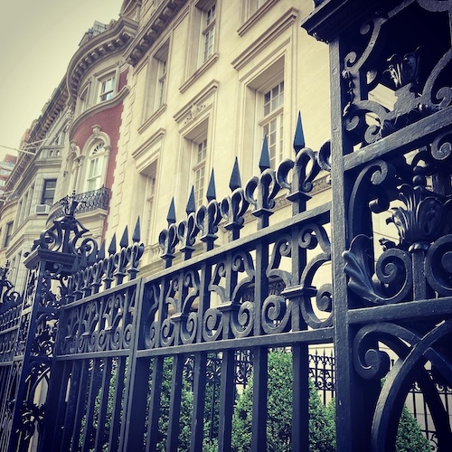 Original photo of a wrought iron fence in New York City. An elaborate black fence with townhouses in the background