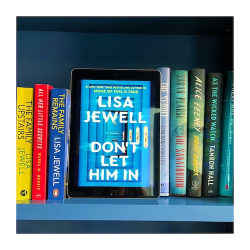 A copy of Don't Let Him in by Lisa Jewell, which shows a blue front door. the book is on a blue shelf next to other Lisa Jewell titles