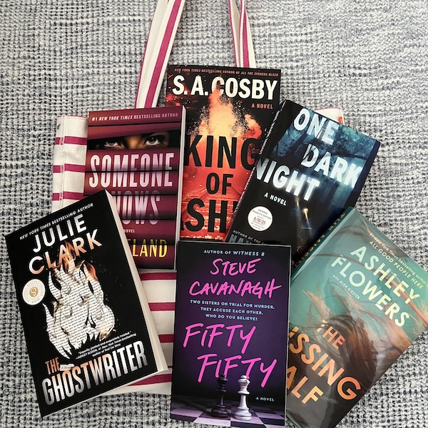 A pink striped tote bag with an array of summer books stacked on it