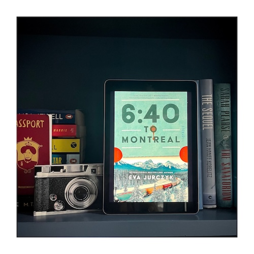 Original photo of the book cover of 640 to Montreal on a navy bookcase next to a camera, passport and other books