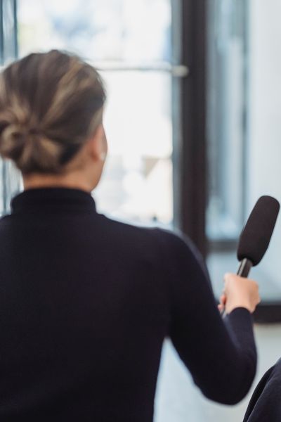 Woman wearing a suit with her hair up holding out a reporter's microphone