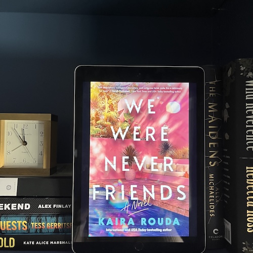 Photo of We Were never Friends on a blue bookcase next to other books and a clock