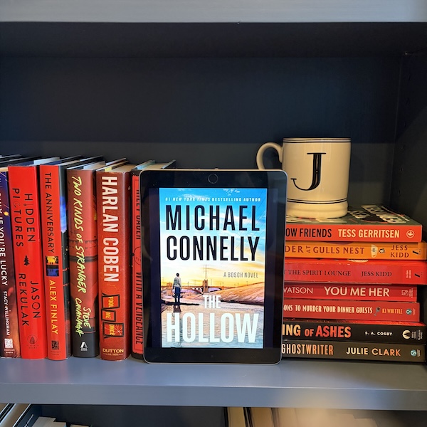 Copy of The Hollow on a shelf of red books and a J mug